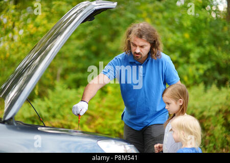 Jeune père et ses filles de vérifier le niveau d'huile dans une voiture familiale Banque D'Images