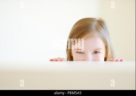 Cute little girl de se cacher sous une table à l'intérieur Banque D'Images