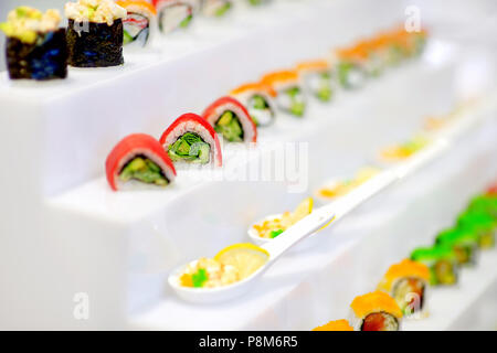 Délicieux sushis avec de l'avocat sur la garniture de fruits de mer et riz roulées disposées en une rangée sur un plateau à un événement Banque D'Images