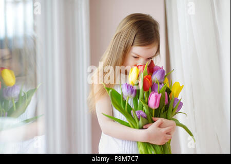 Adorable smiling little girl holding tulipes par la fenêtre Banque D'Images