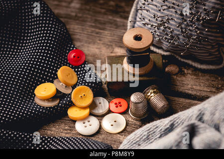 Vue rapprochée de différents boutons colorés parsemés de dés à coudre en bois et tiroir avec fil noir fixé sur planche en bois table avec pièce Banque D'Images