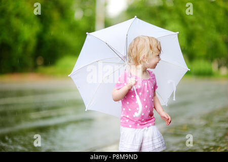 Cute little girl debout dans une flaque d'holding umbrella sur un jour d'été pluvieux Banque D'Images