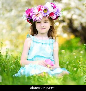 Adorable petite fille portant la couronne de fleurs assis dans blooming cherry garden sur beau jour de printemps Banque D'Images