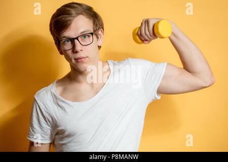 Close up portrait of young sportsman dans les verres montrant ses biceps isolé sur le fond jaune.Temps libre Banque D'Images