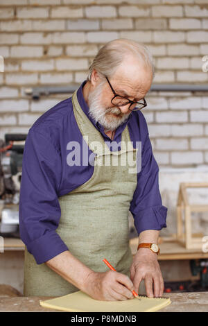 Ancien artisan barbu à lunettes, chemise et tablier faisant un croquis. prendre des notes dans le bloc-notes. closeup portrait Banque D'Images
