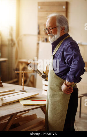 Close up side view portrait d'ancien menuisier avec des cheveux blancs, moustache barbe nad reposant dans l'atelier Banque D'Images