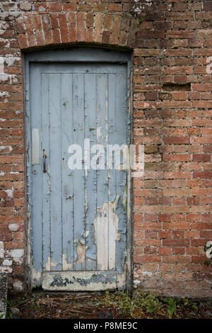 La porte d'un bâtiment en brique à l'abandon qui a été abandonné et mal aimé. Une porte avec de la peinture bleue de déroulage Banque D'Images