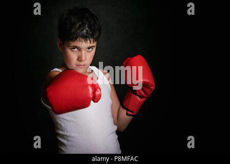 Petit garçon avec des gants de boxe sur fond noir Banque D'Images