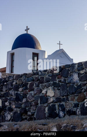 Les dômes de l'église avec de beaux toits bleus typique de Santorin, Grèce. Vue de jour avec immense mur de pierre construit à partir de pierres volcaniques noires Banque D'Images