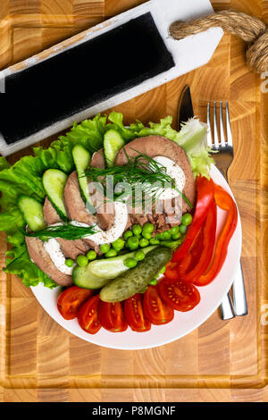 Langue maternelle avec des légumes bouillis tranches de tomates concombre poivron rouge pois laitue avec de la mayonnaise sur la table en bois avec plaque noire. Menu contextuel Banque D'Images