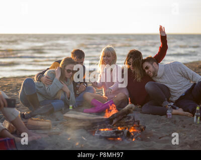 L'insouciance heureuse jeunes amis de s'amuser et de boire une bière par Bonefire sur la plage alors que le soleil commence à définir Banque D'Images