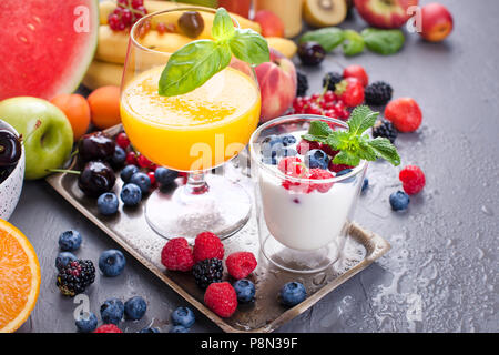 Beaucoup de différents fruits et de baies. Des vitamines et des aliments sains. Produits d'été et jus d'orange dans un verre. Yaourt et muesli avec des baies. Délicieux petit-déjeuner. Copy space Banque D'Images
