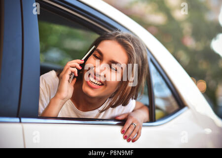 Belle femme avec téléphone en souriant, assis sur le siège arrière de la voiture. Banque D'Images