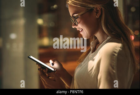 Vue latérale d'happy young woman looking at son téléphone intelligent et souriant. Businesswoman reading text message dans Office. Banque D'Images