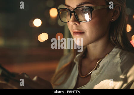 Close up of young woman wearing glasses using cellphone in office. Businesswoman texting sur son téléphone intelligent. Banque D'Images