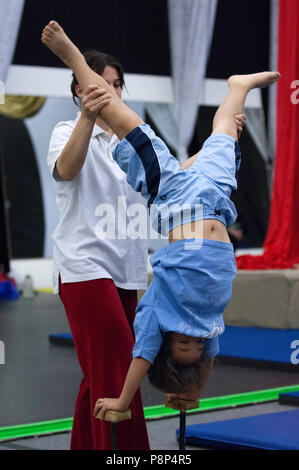 Les pratiques d'un jeune garçon debout sur ses mains en format acrobat school tout en étant repéré par un instructeur. Banque D'Images