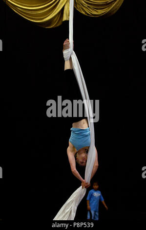 Un jeune garçon regarde une femme acrobat suspend l'envers elle-même avec l'utilisation de soies aériennes. Banque D'Images