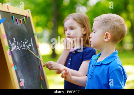 Adorable petite fille jouer a teacher standing par un tableau noir en face de son petit élève Banque D'Images