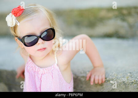 Adorable petite fille portant des lunettes de soleil assis sur les escaliers d'ambiance chaleureuse et ensoleillée journée d'été en ville italienne typique Banque D'Images