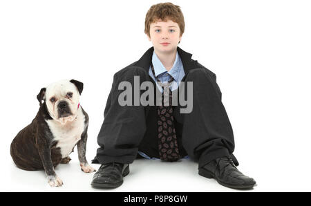 Beau garçon américain de 10 ans en costume baggy assis contre le mur blanc avec Bulldog. Banque D'Images