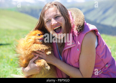 Un petit chien rouge (Spitz Pomeranian) lèche le visage d'une femme en la forçant à rire Banque D'Images