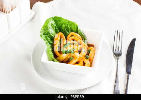 Anneaux de calmars en sauce avec des verts en plaque blanche sur la table de service Banque D'Images