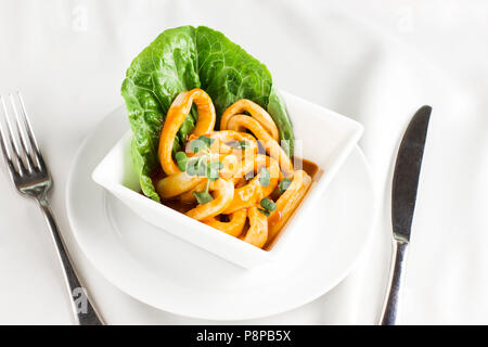 Anneaux de calmars en sauce avec des verts en plaque blanche sur la table de service Banque D'Images