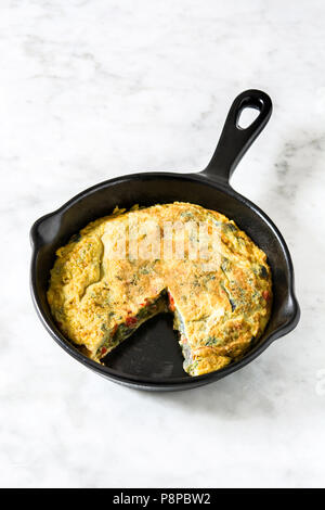 Faites de la frittata des œufs et des légumes dans une poêle de fer, sur le marbre blanc Banque D'Images