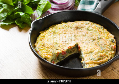 Faites de la frittata des œufs et des légumes dans une poêle de fer, on wooden table Banque D'Images