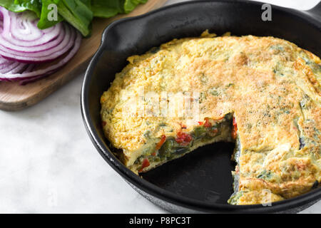 Faites de la frittata des œufs et des légumes dans une poêle de fer, sur le marbre blanc Banque D'Images
