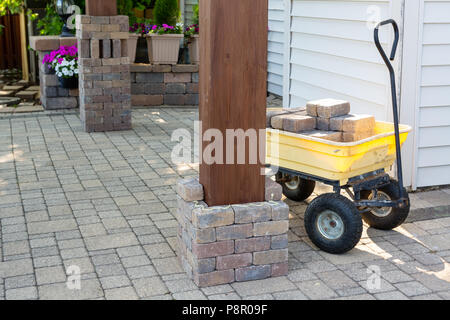 Travaux en cours la construction de piliers en brique sur un patio extérieur pavée entourant les pieds en bois d'un nouveau belvédère Banque D'Images