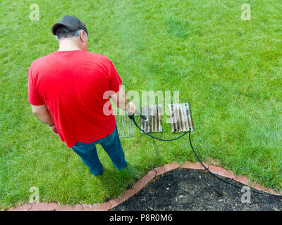 Man spraying une sale barbecue avec un flexible de pression nettoyage des résidus gras avec un puissant jet d'eau sur sa pelouse à la maison Banque D'Images