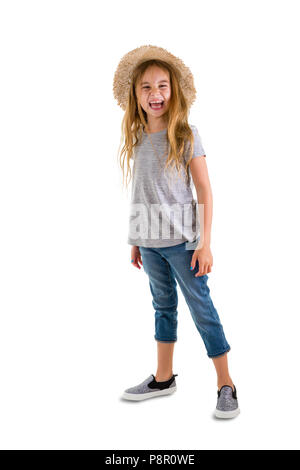 Heureux jolie petite fille blonde avec de longs cheveux blonds ébouriffés portant des jeans à la mode et chapeau de paille pour l'été rire à la caméra dans un port pleine longueur Banque D'Images