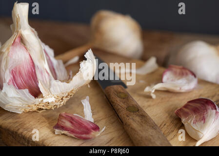 Mauve Bio l'ail et les clous de girofle avec un petit couteau en bois traité en préparation sur une planche à découper en bois Banque D'Images