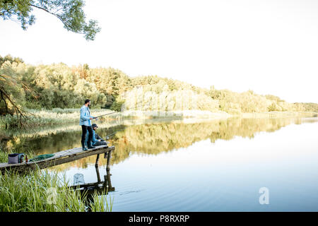 Deux amis de pêche ensemble debout sur la jetée en bois au cours de la lumière du matin sur le bord du lac Banque D'Images