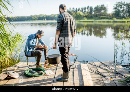 Deux pêcheurs de la préparation de la nourriture pendant le pique-nique sur la jetée en bois près du lac, dans le matin Banque D'Images