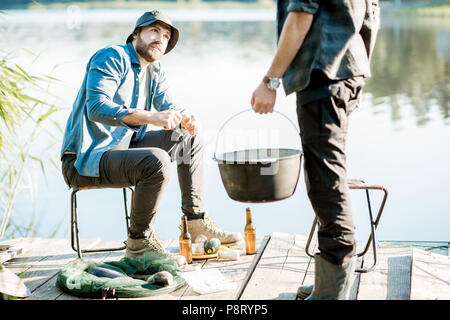 Deux pêcheurs de la préparation de la nourriture pendant le pique-nique sur la jetée en bois près du lac, dans le matin Banque D'Images