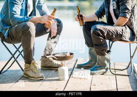 Deux pêcheurs de poissons friture assis avec de la bière pendant le pique-nique sur la jetée en bois près du lac, dans le matin Banque D'Images