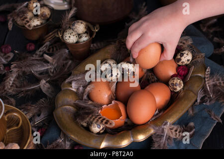 Les mains des enfants dans le cadre d'oeufs de Pâques, grandes et petites, des plumes. Photo dans le style vintage. Accessoires rural. Copy space Banque D'Images