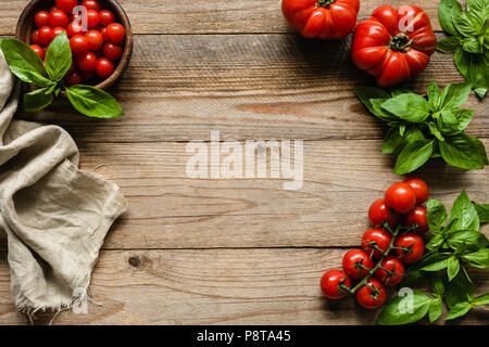 Tomates, basilic et textile sur fond de bois, la cuisson des aliments. Contexte alimentaire rustique avec copie espace. Cadre de l'alimentation Banque D'Images