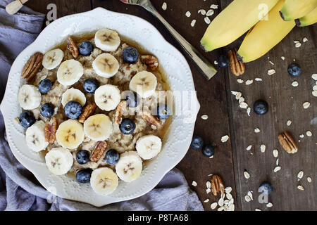 Le petit-déjeuner chaud de gruau sain avec pacanes, bananes, bleuets et de miel sur un fond rustique. Droit coup de frais généraux. Banque D'Images