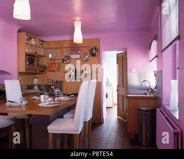 Chaises et table en bois blanc en mauve moderne cuisine salle à manger avec étagères sur mur en bois Banque D'Images