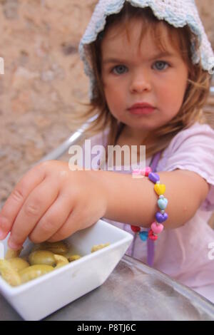 Belle jeune fille douce avec des yeux bleus d'atteindre pour certains d olives un bol en Majorque Banque D'Images