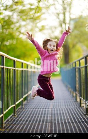 Funny little girl jumping avec joie et bonheur à l'extérieur sur beau jour d'été Banque D'Images