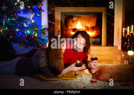 Heureux couple pose par une cheminée dans un confortable salon sombre la veille de Noël Banque D'Images