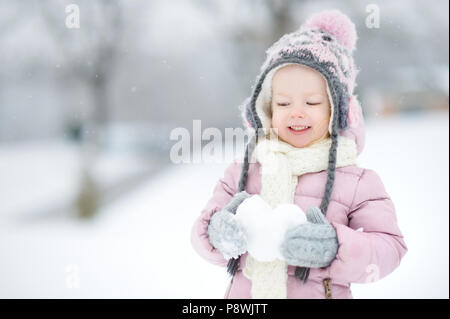 Funny little girl holding snow coeur dans le magnifique parc de neige pendant l'hiver Banque D'Images