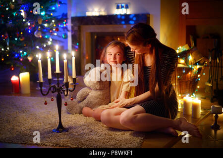 Jeune mère et sa petite fille assise au coin d'une cheminée dans un confortable salon sombre la veille de Noël Banque D'Images