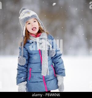 Funny little girl attraper des flocons avec sa langue dans le magnifique parc de neige pendant l'hiver Banque D'Images