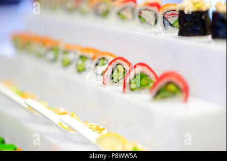 Délicieux sushis avec de l'avocat sur la garniture de fruits de mer et riz roulées disposées en une rangée sur un plateau à un événement Banque D'Images