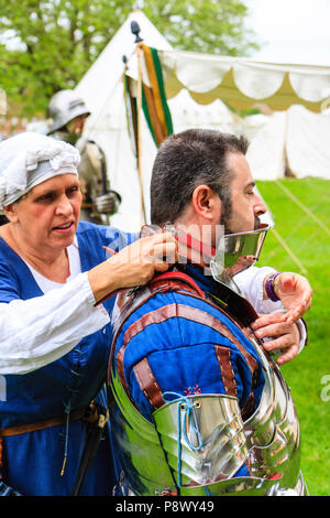 Re-enactment, histoire vivante. Femme en costume médiéval à base de flambage sur casque pour knight comme elle l'aide à s'habiller en armure. Banque D'Images